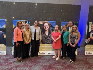 A group of firm employees gathered around a poster of award recipient Jennifer Hardin